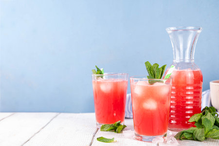 Homemade watermelon lemonade, sweet refreshing summer drink, iced watermelon juice with mint decor and striped straw, light blue and wooden background, copy spaceの写真素材
