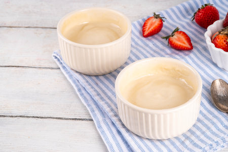 Vanilla or white chocolate pudding dessert, in ceramic portioned bowl on kitchen table, with fresh strawberriesの写真素材