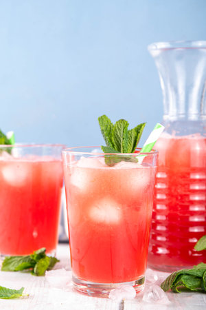 Homemade watermelon lemonade, sweet refreshing summer drink, iced watermelon juice with mint decor and striped straw, light blue and wooden background, copy spaceの写真素材