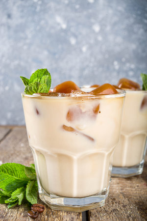 Cold summer coffee, latte, frappe. Coffee iced cocktail drink with frozen coffee ice cubes, milk or non-dairy milk and mint leaves. Wooden background copy spaceの写真素材