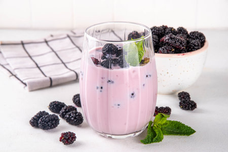 Mulberry shake, smoothie or yogurt drink on portioned glass, with a lot of fresh organic mulberry berries and mint, on white kitchen table, copy spaceの写真素材