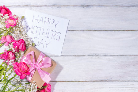 Moms day greeting card, invitation background, Spring bouquet of beautiful ranunculus flower, with cute craft paper gift bow and note Happy Mothers day, copy space on white backgroundの写真素材
