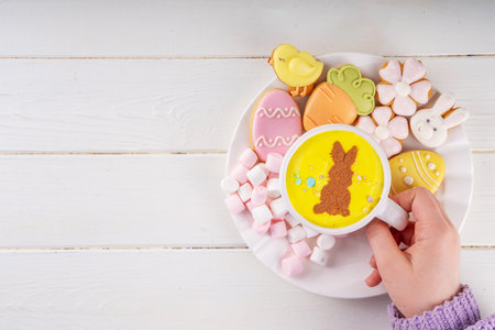 Hot sweet drinks for Easter party, breakfast, lunch. Easter menu. Pink, yellow, blue, brown multicolored hot chocolate cups with marshmallows, chocolate drawing rabbit, Easter eggs on latte surfaceの写真素材