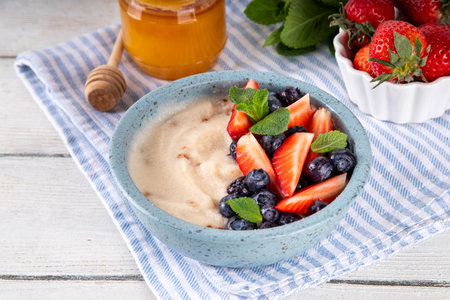 Cream of Wheat semolina porridge with fresh summer berry. Portion of breakfast whole grain creme de semolina with dairy milk, strawberry, blueberry and honeyの写真素材