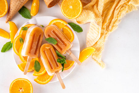 Homemade orange creamsicle lolipop ice cream, creamsicle popsicles, with orange slices and mint, sweet creamy summer dessert, on white kitchen table copy spaceの写真素材