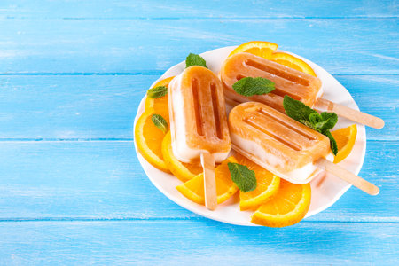 Homemade orange creamsicle lolipop ice cream, creamsicle popsicles, with orange slices and mint, sweet creamy summer dessert, on white kitchen table copy spaceの写真素材