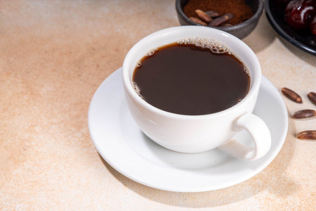 Healthy organic date seed coffee, black coffee cup, made with grated date seeds, with whole date fruits and seeds on beige background . Alternative coffee hot drinkの写真素材