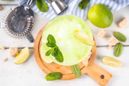 Mojito lemonade alcoholic slush cocktail, in a martini glass, summer refreshing slushy drink with vodka, lime juice and mint syrup, on a white table with bar utensilsの写真素材