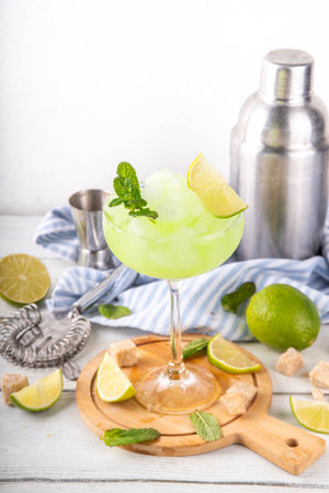 Mojito lemonade alcoholic slush cocktail, in a martini glass, summer refreshing slushy drink with vodka, lime juice and mint syrup, on a white table with bar utensilsの写真素材