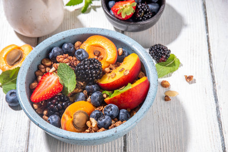 Granola breakfast with fruit and berry, summer whole grain tasty breakfast bowl with a lot of fruit and berries, with milk jug on white wooden tableの写真素材