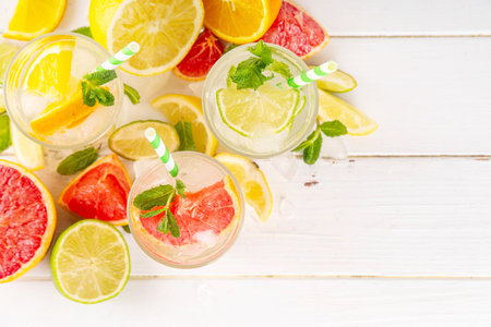 Set of summer citrus infused detox water drinks, lemon, lime, grapefruit, orange, lime iced lemonade drinks on white wooden background. Iced seasonal refreshment beverages, with fruit slices and mintの写真素材