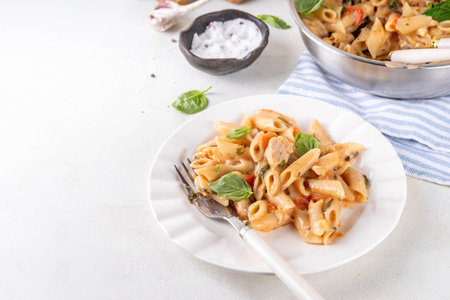 Trendy viral marry me chicken pasta. One pot balanced tender cooked pasta and juicy chicken pieces smothered in creamy and cheesy, garlic sun-dried tomato sauce, wit basil leaves, in plate and potの写真素材