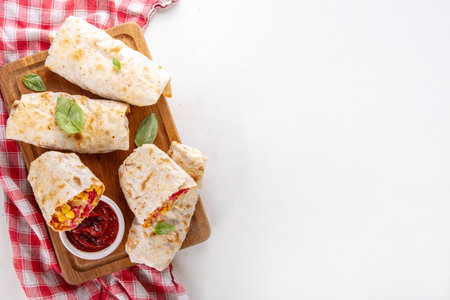 Homemade oven baked Pizza Burritos, pizza style quesadilla wraps with pepperoni or salami, tomatoes, cheese and corn, on kitchen table with hot tomato sauce, copy spaceの写真素材