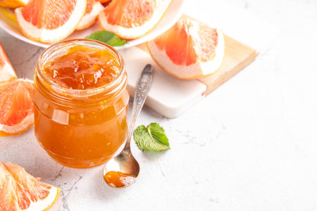 Homemade grapefruit jam, sweet pink grapefruit marmalade in small jar, with grapefruit slices and mint leaves on white table backgroundの写真素材
