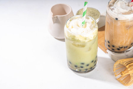 Classic and green matcha boba bubble tea with tapioca pearls and whipped non-dairy creamer on top of glass, summer cold sweet dessert drink on white table background copy spaceの写真素材