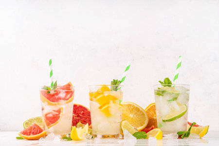 Set of summer citrus infused detox water drinks, lemon, lime, grapefruit, orange, lime iced lemonade drinks on white wooden background. Iced seasonal refreshment beverages, with fruit slices and mintの写真素材