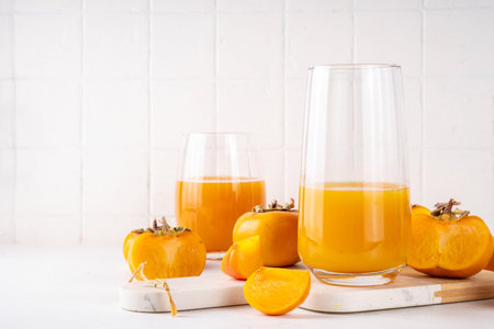Fresh homemade persimmon juice in portioned glasses, with whole and cut persimmon c in the backgroundの写真素材