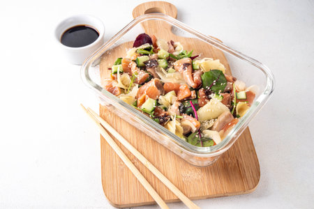 Healthy balanced sushi bowl lunch box with rice, nori, cucumbers, lettuce leaves, salmon fish and sesame, soy sauce and chopsticksの写真素材