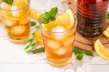 Iced tea cocktail drink, cold summer drink with black tea, lemon, mint and crushed ice, tasty refreshing non-alcohol mocktail on white wooden table backgroundの写真素材