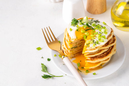 Tasty savory breakfast pancakes with spring green onion and fried eggs. Stack or delicious non-sweet pancakes with scallons, parsley and sunny side up eggs, on white kitchen table copy spaceの写真素材