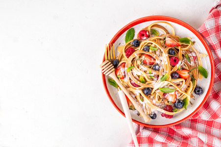 Spaghetti pancakes with fresh berries, summer sweet breakfast or lunch recipe idea, homemade Pancake make in form of spaghetti with powdered sugar and honey, on white kitchen tableの写真素材