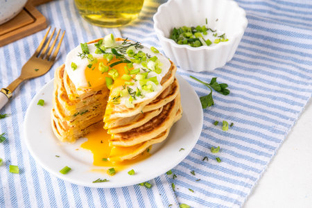 Tasty savory breakfast pancakes with spring green onion and fried eggs. Stack or delicious non-sweet pancakes with scallons, parsley and sunny side up eggs, on white kitchen table copy spaceの写真素材
