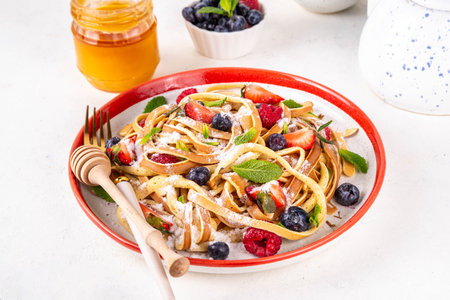 Viral trendy spaghetti pancakes with fresh berries, summer sweet breakfast or lunch recipe idea, homemade Pancake make in form of spaghetti with powdered sugar and honey, on white kitchen tableの写真素材