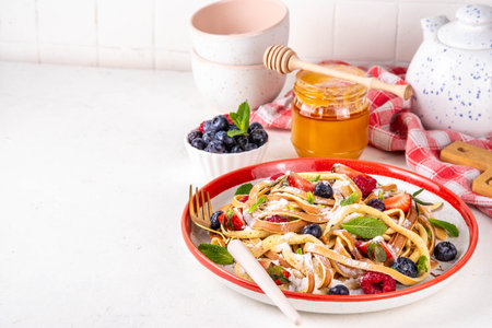 Viral trendy spaghetti pancakes with fresh berries, summer sweet breakfast or lunch recipe idea, homemade Pancake make in form of spaghetti with powdered sugar and honey, on white kitchen tableの写真素材
