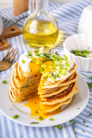 Tasty savory breakfast pancakes with spring green onion and fried eggs. Stack or delicious non-sweet pancakes with scallons, parsley and sunny side up eggs, on white kitchen table copy spaceの写真素材