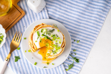 Tasty savory breakfast pancakes with spring green onion and fried eggs. Stack or delicious non-sweet pancakes with scallons, parsley and sunny side up eggs, on white kitchen table copy spaceの写真素材
