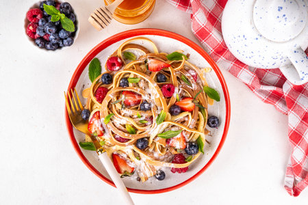 Viral trendy spaghetti pancakes with fresh berries, summer sweet breakfast or lunch recipe idea, homemade Pancake make in form of spaghetti with powdered sugar and honey, on white kitchen tableの写真素材