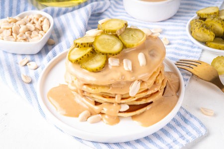 Peanut butter Pickle Pancakes. Stack of fluffy tasty savory Pancakes wit a lot of Peanut butter drizzle, peanuts and pickles, copy spaceの写真素材