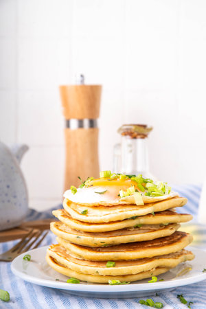 Tasty savory breakfast pancakes with spring green onion and fried eggs. Stack or delicious non-sweet pancakes with scallons, parsley and sunny side up eggs, on white kitchen table copy spaceの写真素材