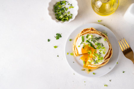 Tasty savory breakfast pancakes with spring green onion and fried eggs. Stack or delicious non-sweet pancakes with scallons, parsley and sunny side up eggs, on white kitchen table copy spaceの写真素材