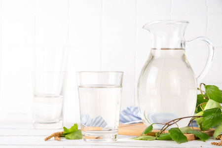 Birch sap in jar and glass, freshly made organic birch juice, sweet natural drink, on white wooden background with birch tree twigsの写真素材