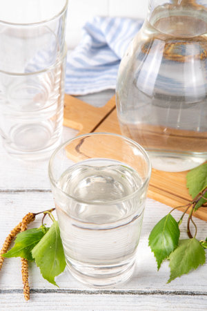 Birch sap in jar and glass, freshly made organic birch juice, sweet natural drink, on white wooden background with birch tree twigsの写真素材