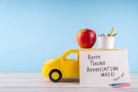 Teacher Appreciation Week background with school supplies and traditional gifts, bouquet of spring flowers with pens, pencils, notebooks, notepads, school bus toy, greeting card to teacher from childの写真素材