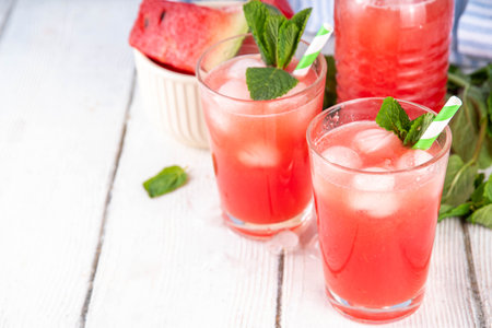 Homemade watermelon lemonade, sweet refreshing summer drink, iced watermelon juice with mint decor and striped straw, light blue and wooden background, copy spaceの写真素材