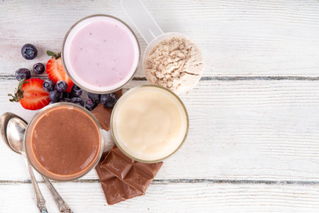 Quick and simple protein pudding. Healthy summer cold dessert. Three glasses with vanilla, chocolate and berry protein pudding, with chocolate slices, fresh strawberry, blueberry, protein powder scoopの写真素材