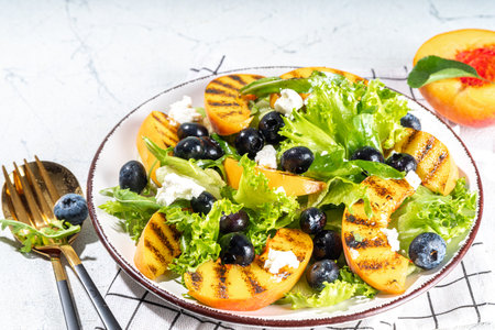 Summer peach salad. Fresh raw green salad with lettuce, arugula, grilled peach wedges, blueberry, feta cheese and honeyの写真素材