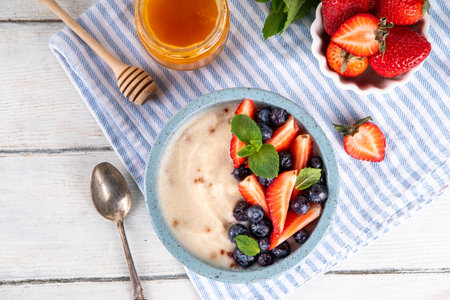 Cream of semolina porridge with fresh summer berry. Portion of breakfast whole grain creme de semolina with dairy milk, strawberry, blueberry and honeyの写真素材