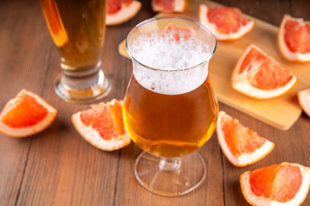 Glasses with Sour Grapefruit Craft Beer or Ale on wooden table with fresh pink grapefruit slicesの写真素材