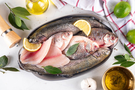 Raw fish and seafood cooking background, various fresh whole and sliced fish with spices, lemon, olive oil for preparation dinner, white table background copy spaceの写真素材
