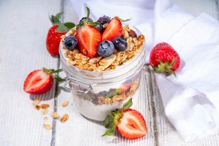 Summer berries granola breakfast layered dessert with yogurt, oat multi grain granola, strawberry, blueberry on wooden table background copy spaceの写真素材