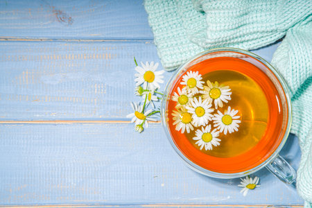 Cup of brewed chamomile tea with bouquet of chamomile daisy, blue wooden background copy space. Herbal organic drink.の写真素材