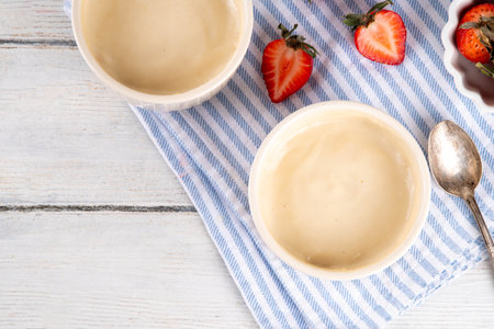 Vanilla or white chocolate pudding dessert, in ceramic portioned bowl on kitchen table, with fresh strawberriesの写真素材
