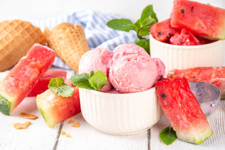Homemade watermelon ice cream, sweet red melon sorbet gelato in portioned bowl, with watermelon slices and mint on white wooden table backgroundの写真素材
