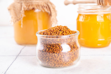 Bee pollen jar and spoon with honey and honeycomb. Trendy superfood, antioxidant organic powder, on white table background copy spaceの写真素材