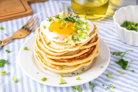 Tasty savory breakfast pancakes with spring green onion and fried eggs. Stack or delicious non-sweet pancakes with scallons, parsley and sunny side up eggs, on white kitchen table copy spaceの写真素材
