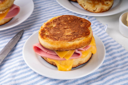 Breakfast crumpet sandwich, british pancake scones burger with cheese and ham, on itchen table, with stack of crumpets and butterの写真素材